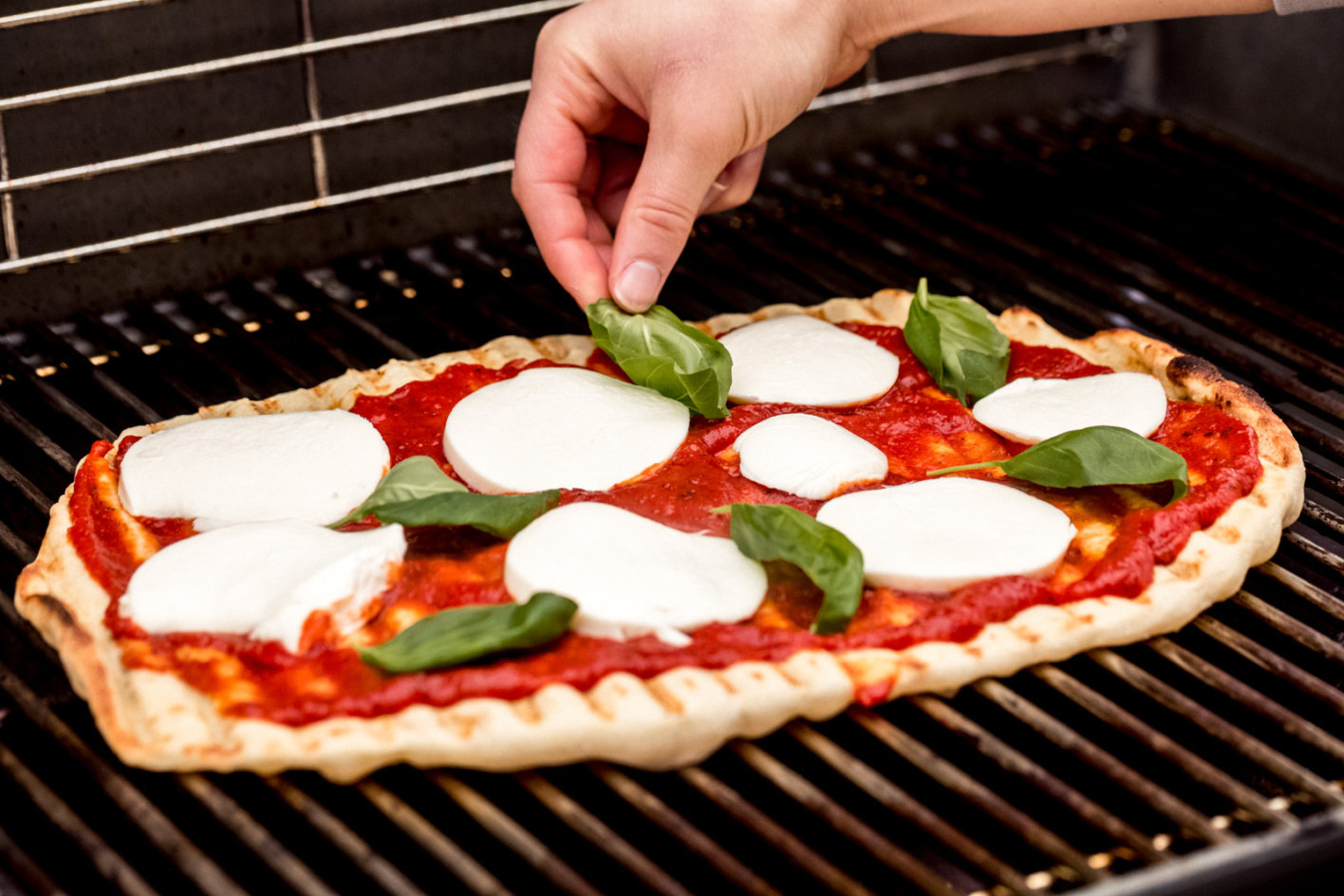 A margarita pizza topped with tomato sauce, mozzarella, and fresh basil on a grill. 