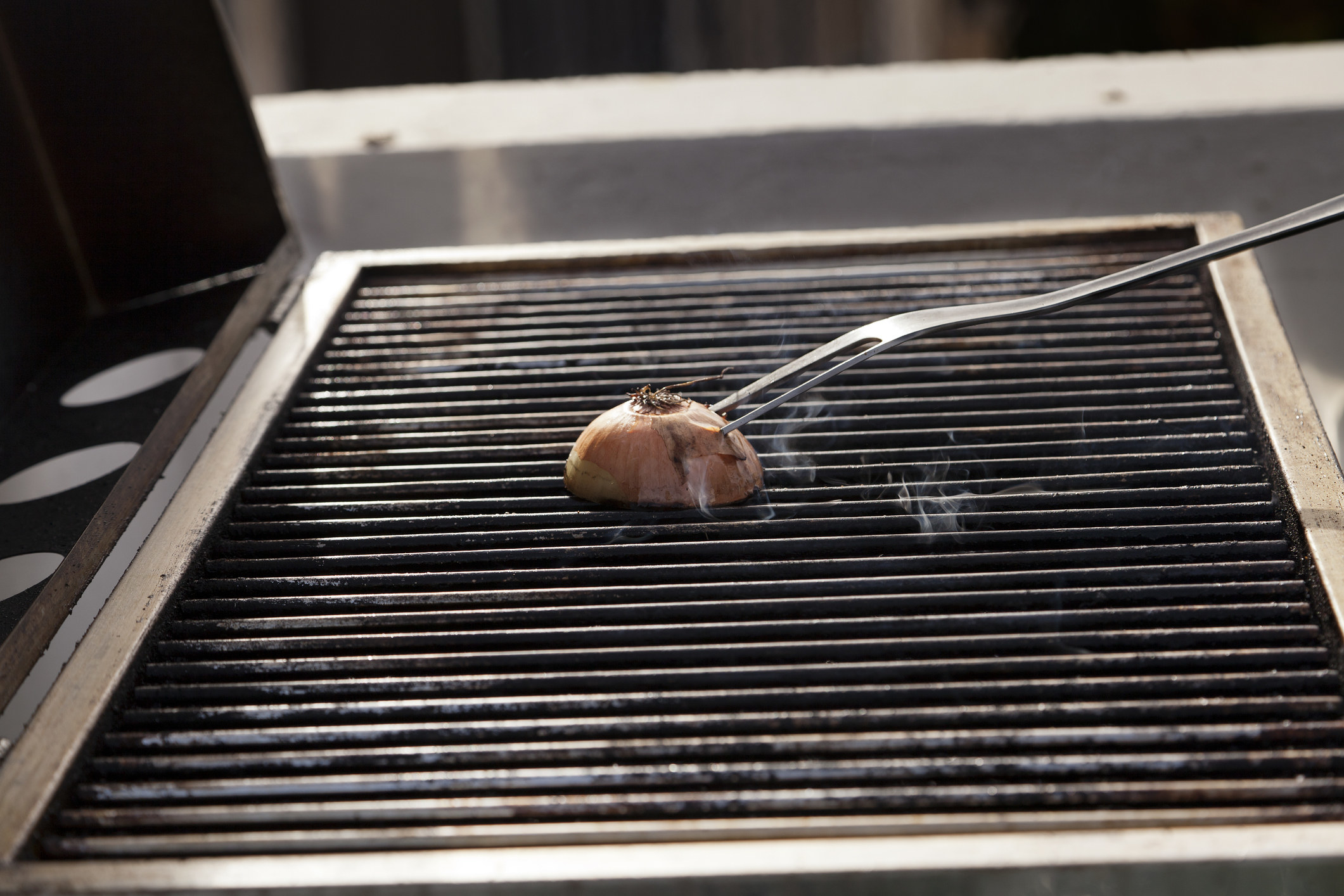 A long grilling fork piercing a halved onion to clean the grates of a grill.