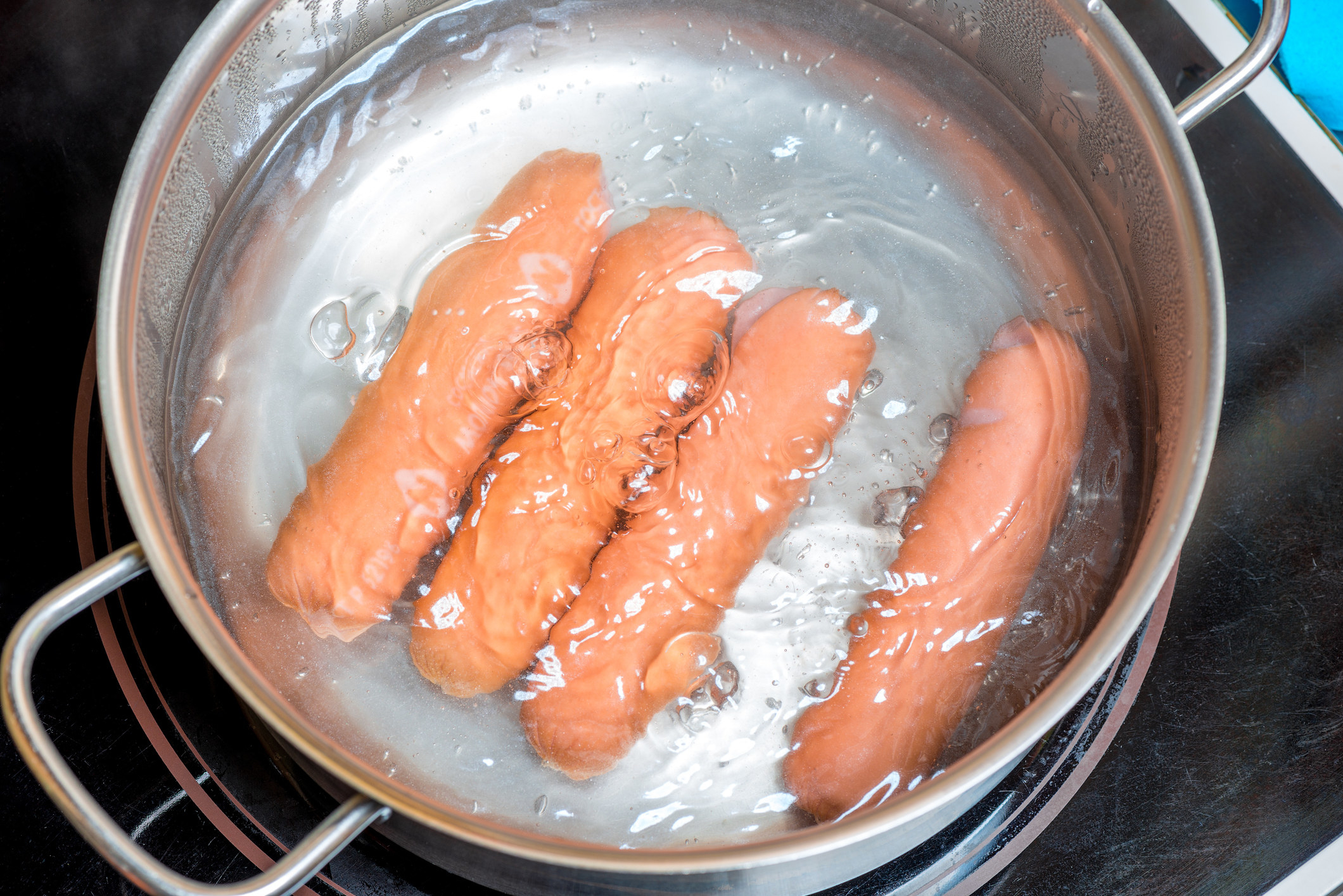 Hot dogs being poached in hot water in a sauce pan.