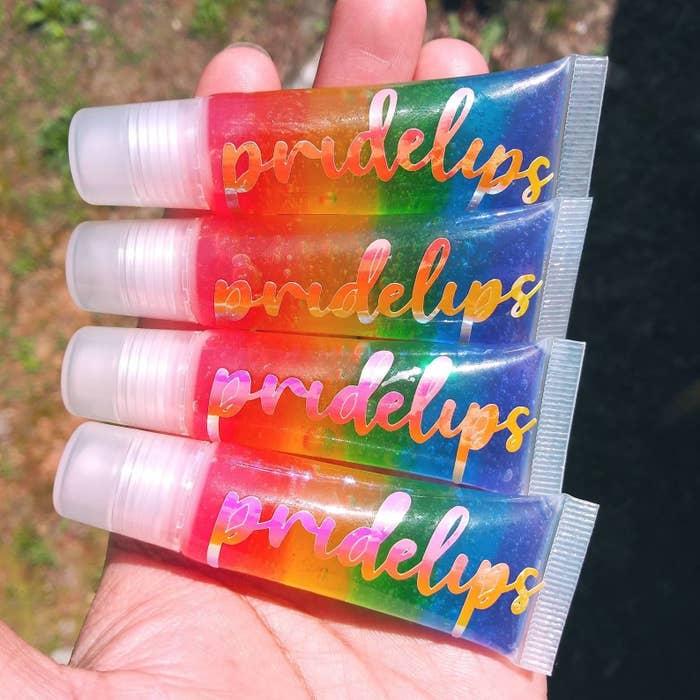 Four tubes of lip gloss with rainbow gloss inside and &quot;pridelips&quot; printed on the front in a model&#x27;s hands