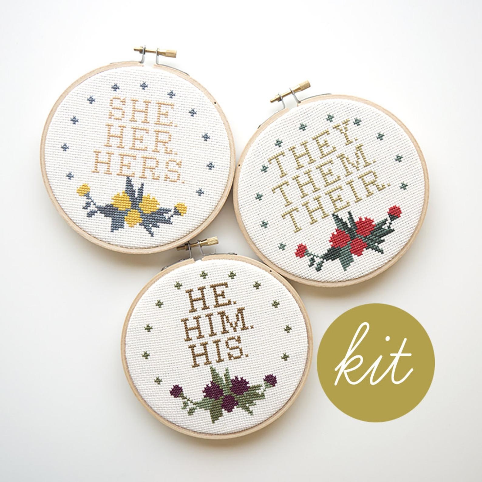 Three cross stitch loops, all with small floral design at the bottom and the one on the top left has the words &quot;Sher, Her, Hers&quot; the top right has the words &quot;They, Them, Their&quot;, and the one in the middle bottom has the words &quot;He, Him, His&quot;