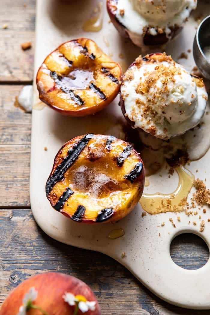 Grilled peaches on a serving platter with cream and cinnamon crumble.