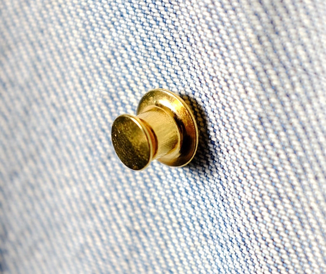 A gold pin backing on the inside of a denim jacket