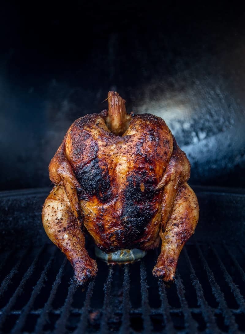 A whole chicken propped up on a can of wine cooking on the grill. 