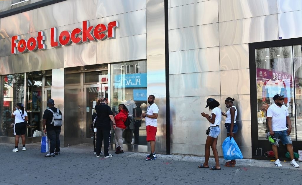 People wait in line to enter a Foot Locker store