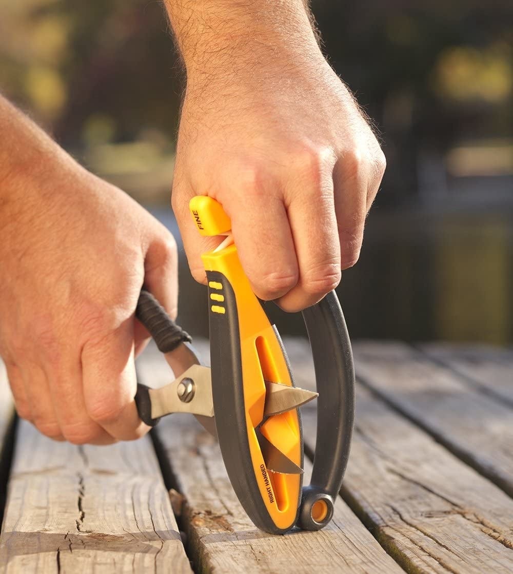 A person using the handheld sharpener to sharpen their scissors