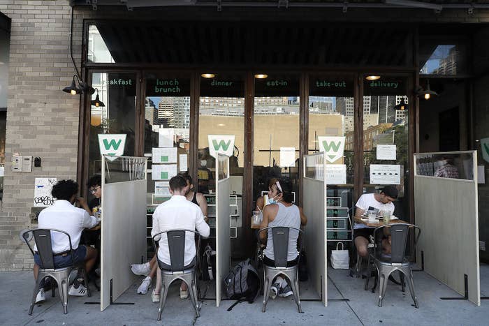 Diners eat their meals separated by dividers in an outdoor restaurant seating area