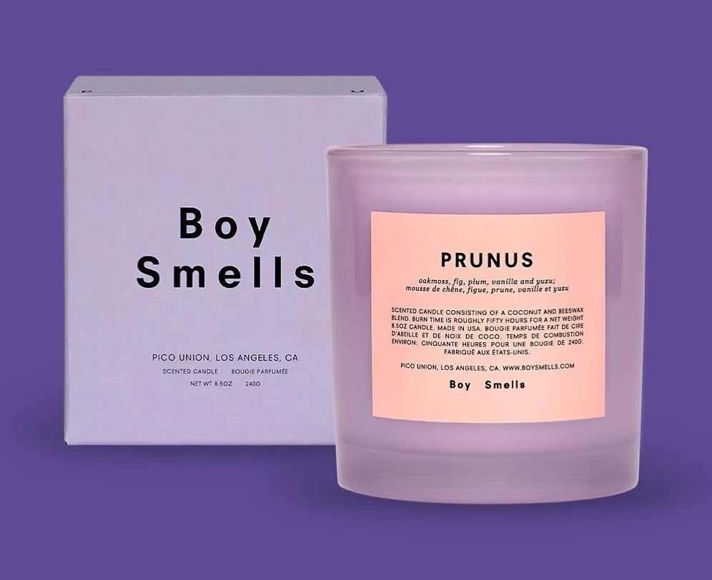 蜡烛在紫色的持有人的标题“Prunus"和气味笔记和一盒旁边的字“男孩Smells"在它上面