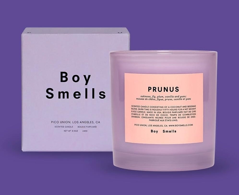 Candle in purple holder with the title "Prunus" and smell notes on it with a box next to it with the word "Boy Smells" on it