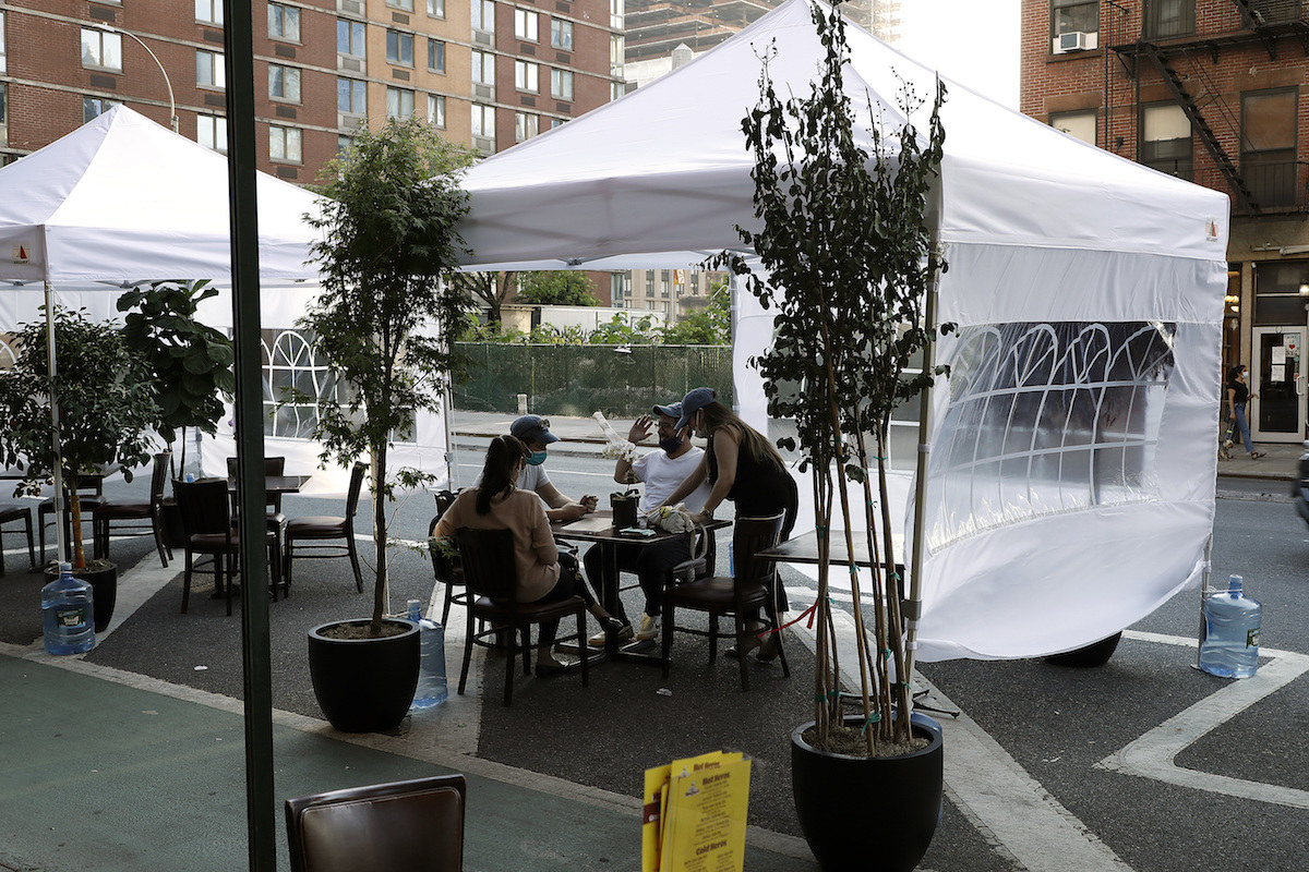 Diners enjoy their meals beneath tents in an outdoor restaurant seating area