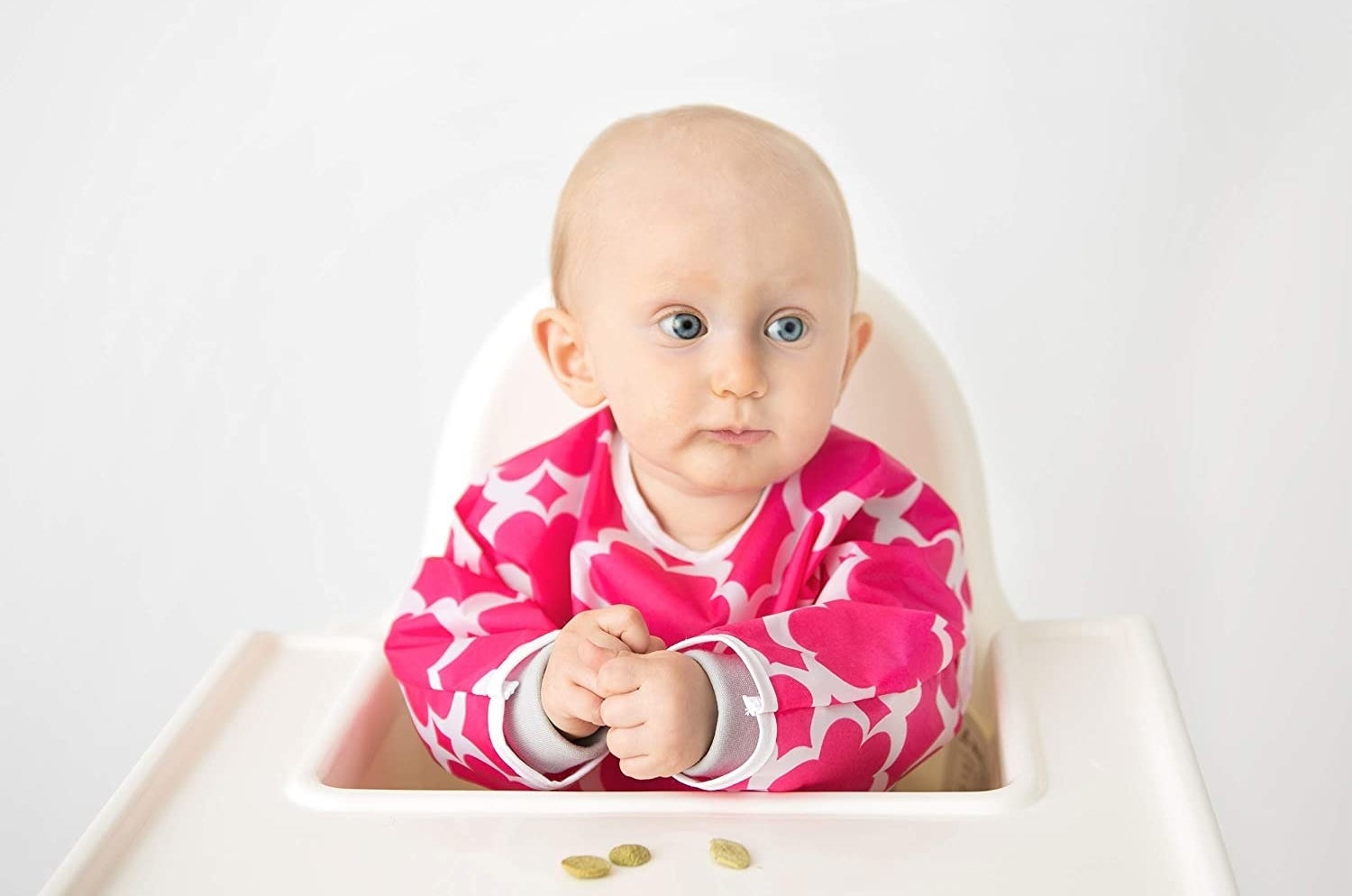 A baby sitting in a high chair with a bib on The bib has long sleeves