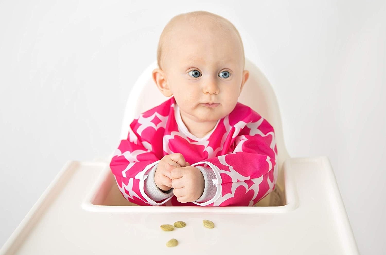 A baby sitting in a high chair with a bib on The bib has long sleeves