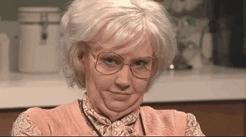 Kate McKinnon winks and raises her eyebrows dressed up as an old lady