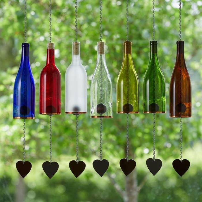Seven wine bottles that have been transformed into wind chimes with hearts at the end of each chain