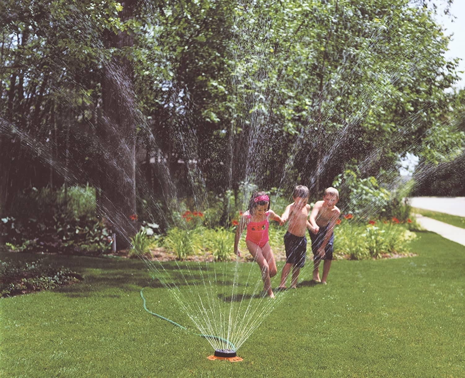 kids running through small round sprinkler spraying water in all directions