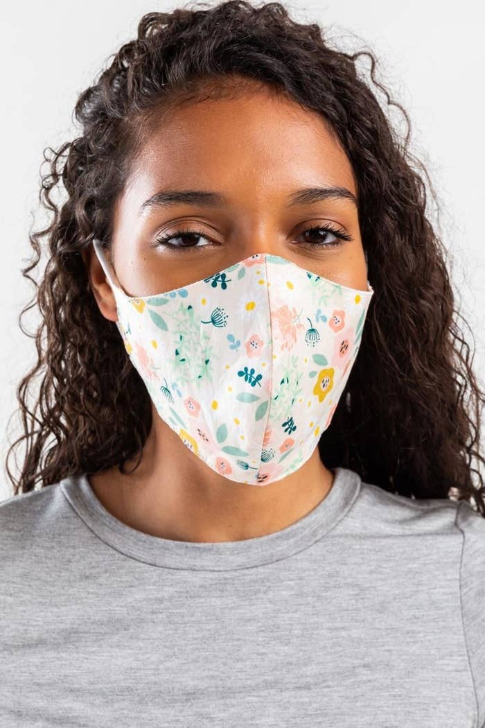 model wearing a face mask with ear loops and a pastel floral print on a white background