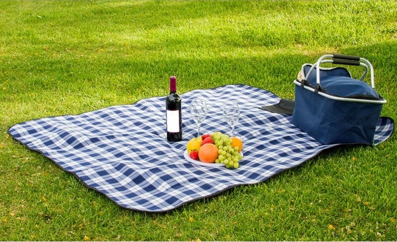 A blue plaid picnic blanket unfolded on a lawn