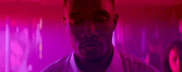 Frank Ocean looks like he is in a club with pink and purple lighting. He slowly opens his eyes over and over, because this is a GIF.