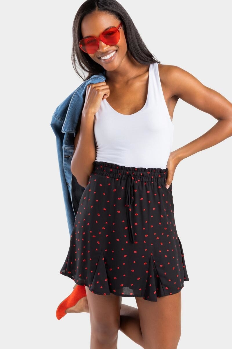 model wearing a white tank top tucked into black high-waist A-line skirt with tiny red lips print on it