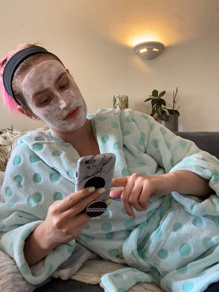 Me sitting on the couch in a robe, with a clay mask on my face, scrolling on my phone.