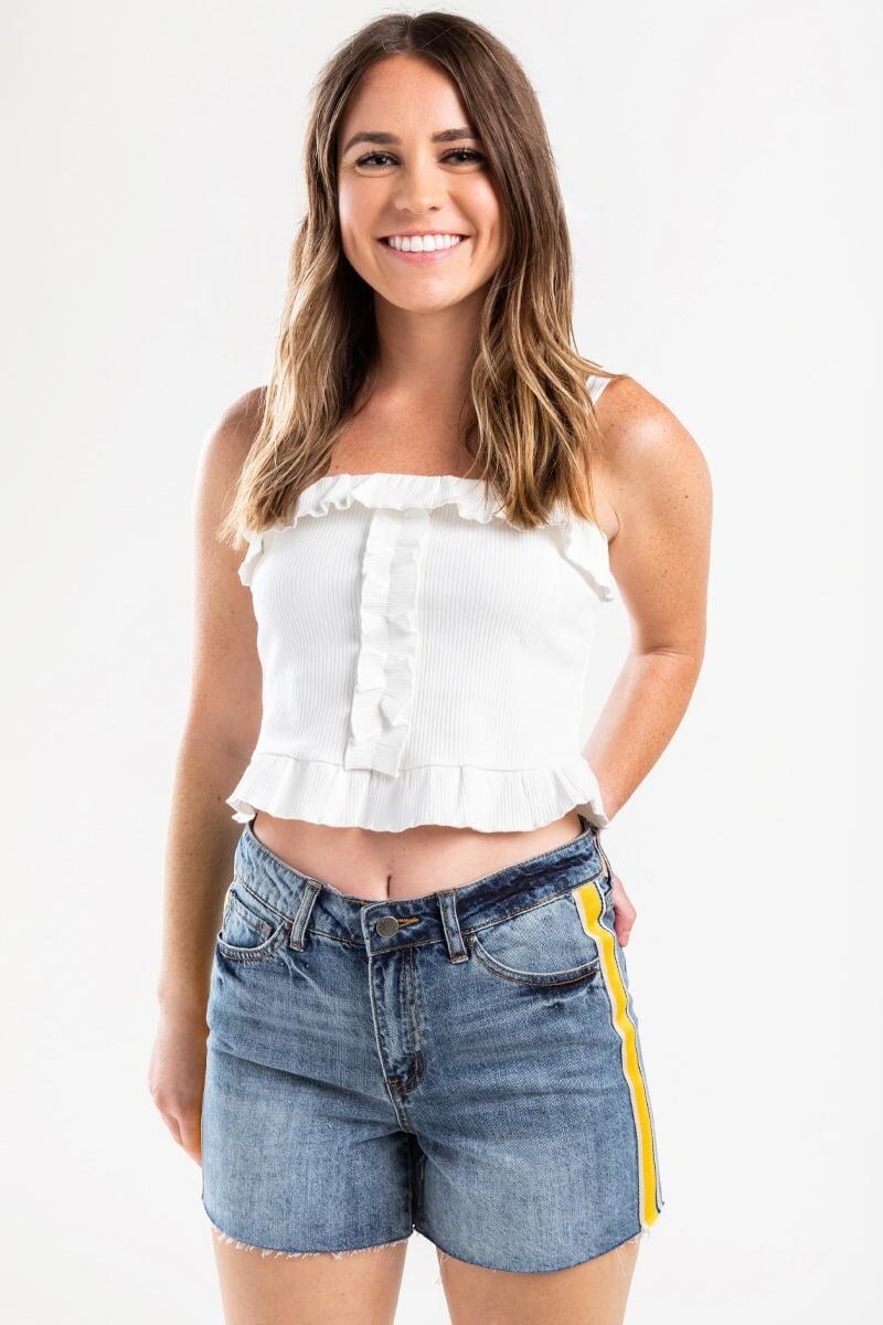 model wearing a white crop top with denim shorts that have some weathering and a bright yellow ribbon strip down the side