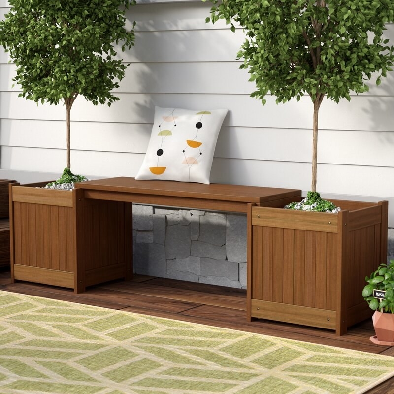 A walnut brown wooden bench with planters on either side of it