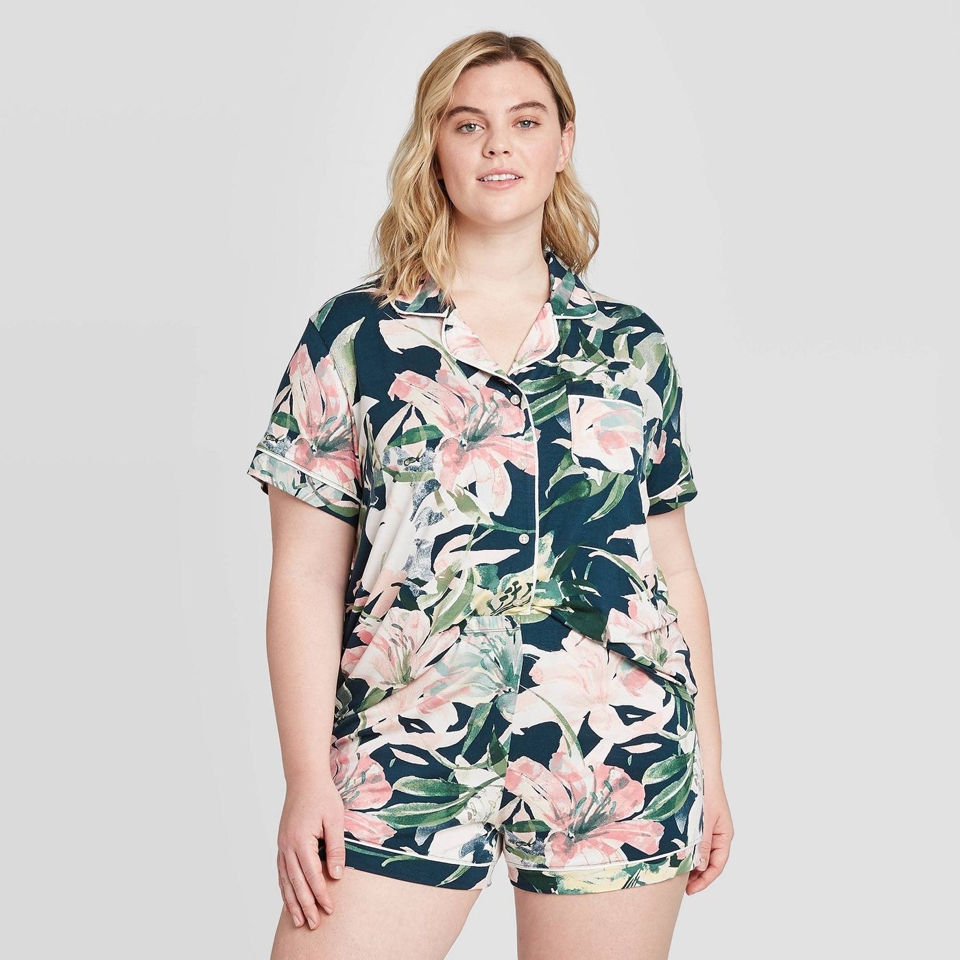 A model in a short sleeve tee and matching pajama short in dark green with pink floral watercolor patterns 