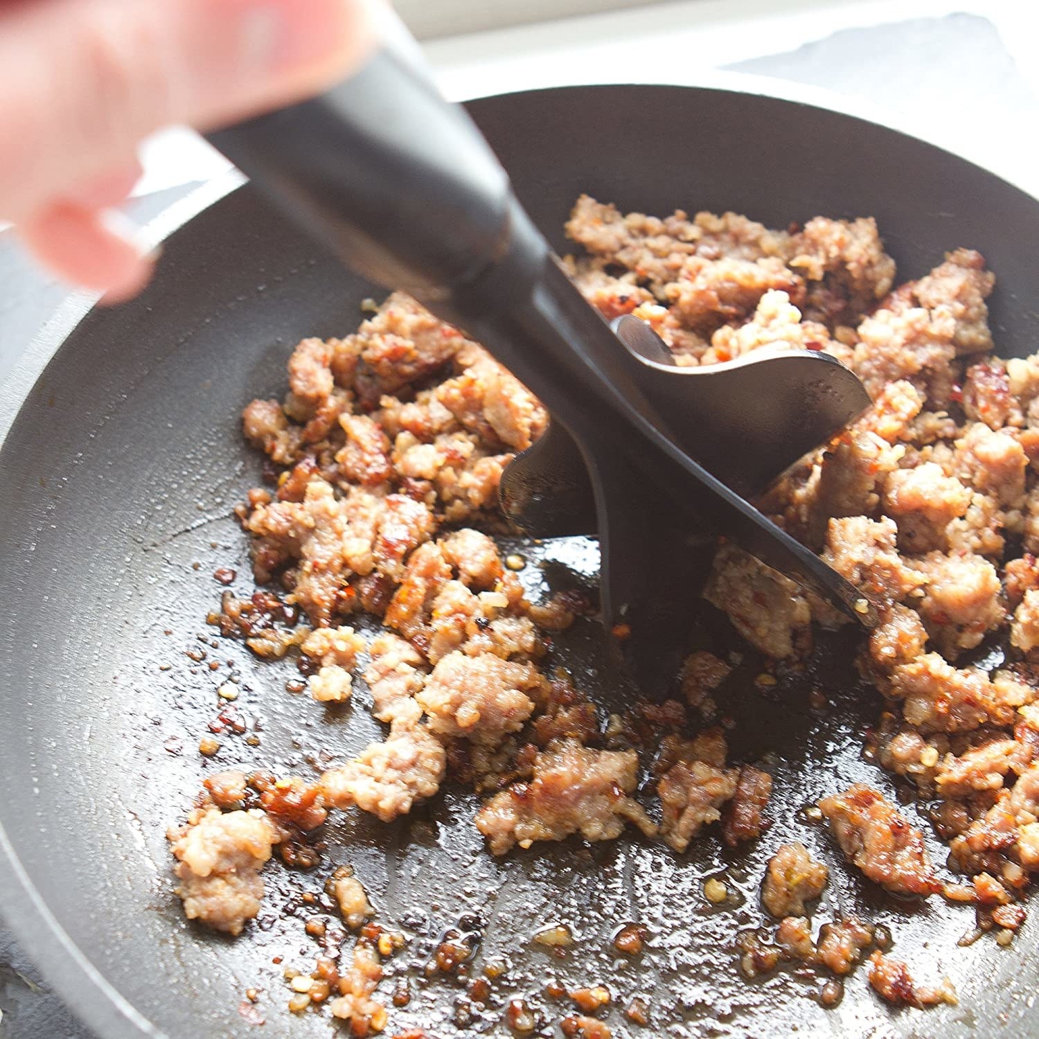 A tool breaks up ground beef in a skillet
