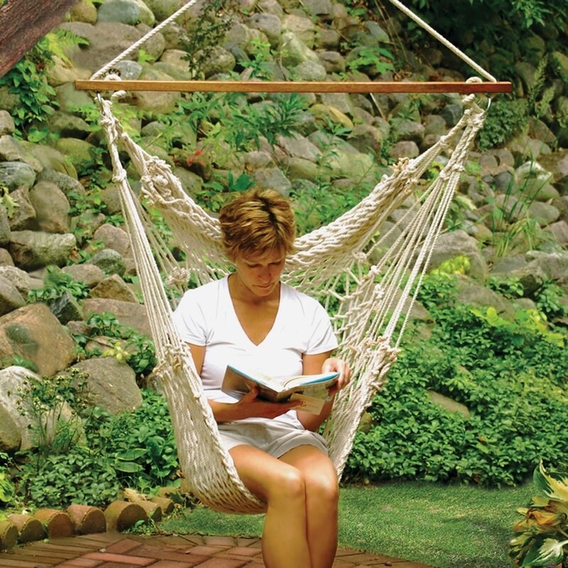 A model reading a book while sitting outdoors in a white rope hanging hammock