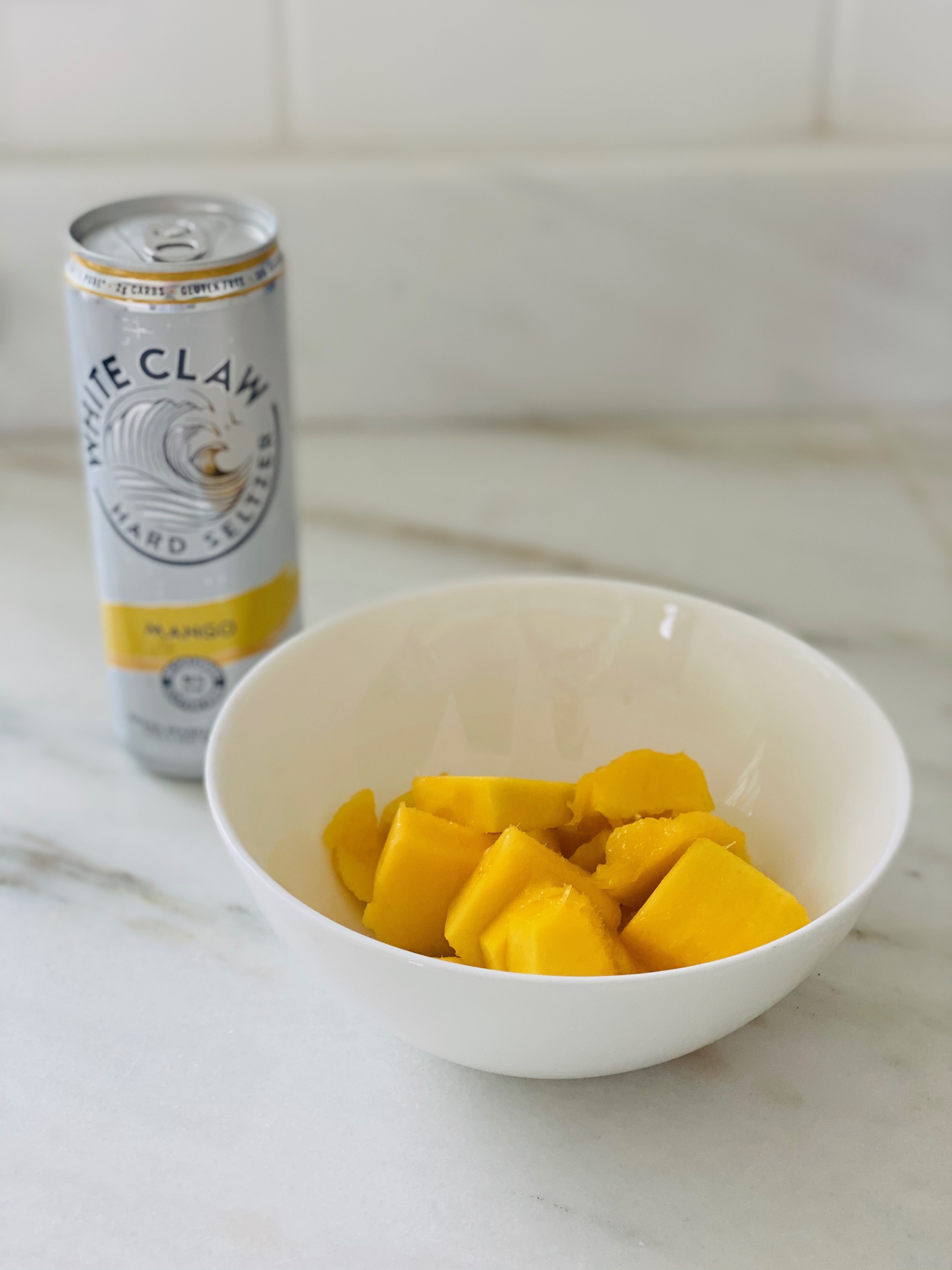 A bowl of sliced mangos and a mango White Claw in the background.