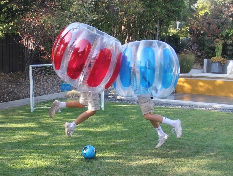 Two models wearing large clear inflatable balloons, one red, the other blue, playfully slamming into each other