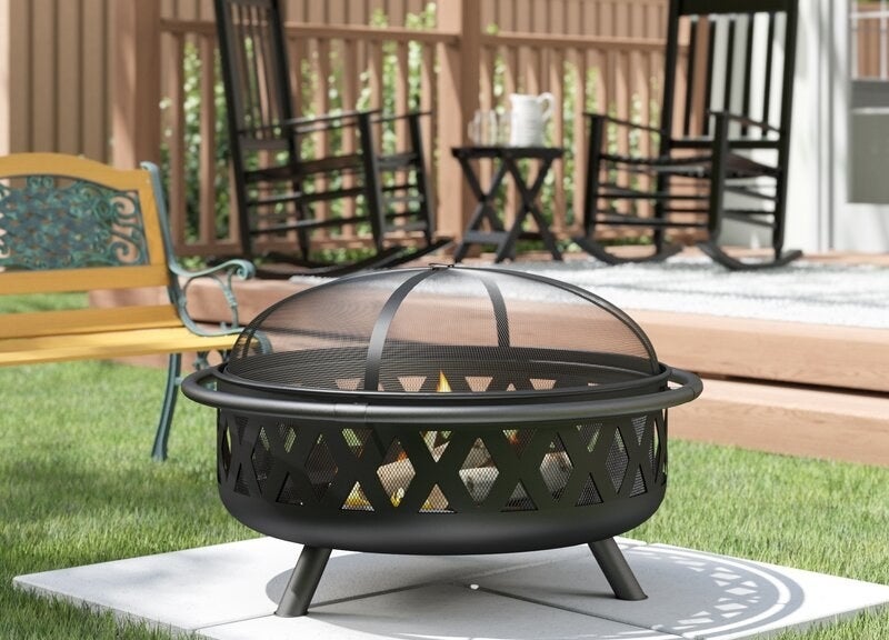 A covered black steel fire pit with logs on fire inside of it