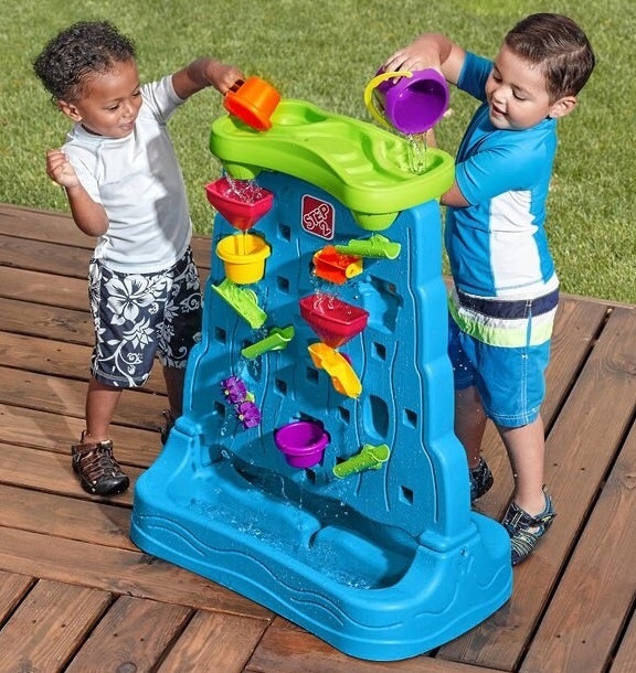 Two child models pouring water and playing with a bright blue plastic water table
