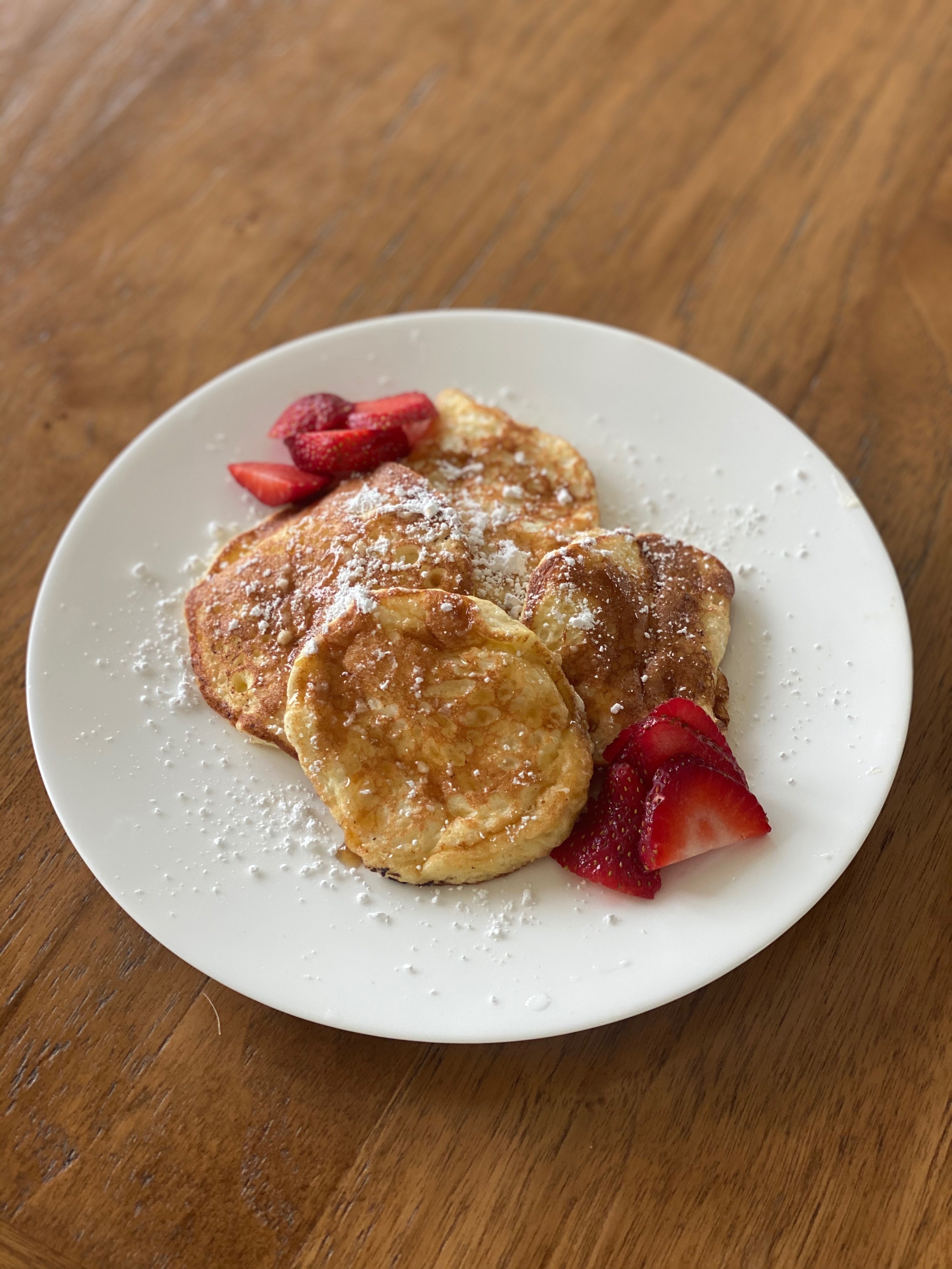 A plate of fluffy Japanese-style pancakes topped with powdered sugar, a drizzle of maple syrup, and sliced strawberries on the side.