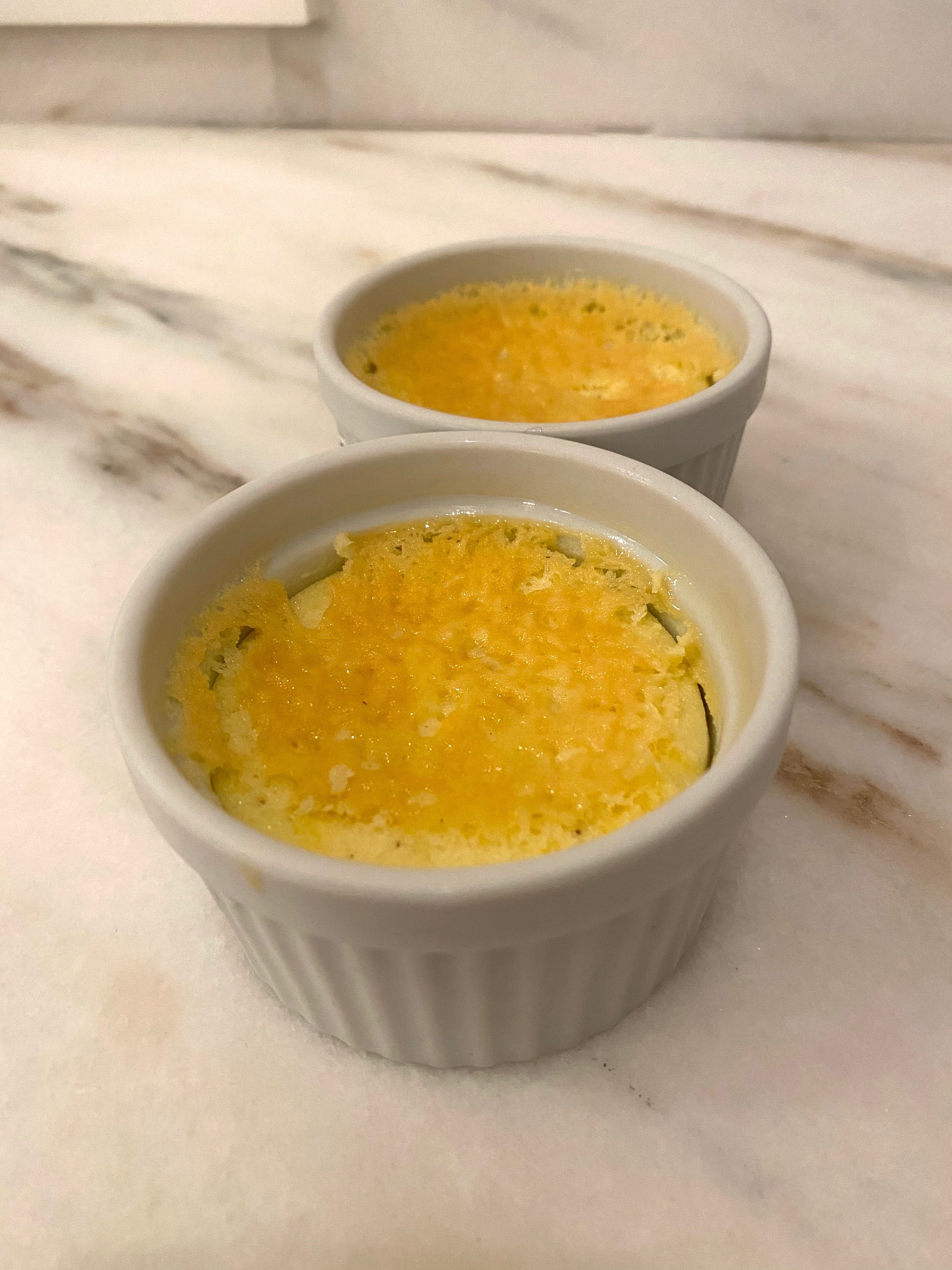 Two ramekins filled with the crème brûlée mixture on a countertop. 