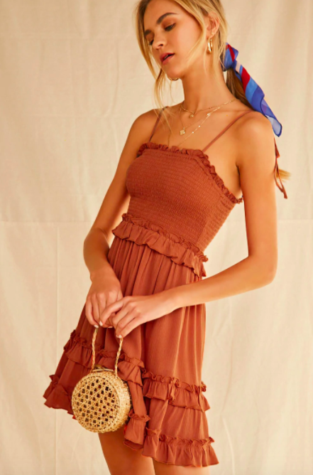 Model wears a rust-colored sleeveless tiered dress with ruffles