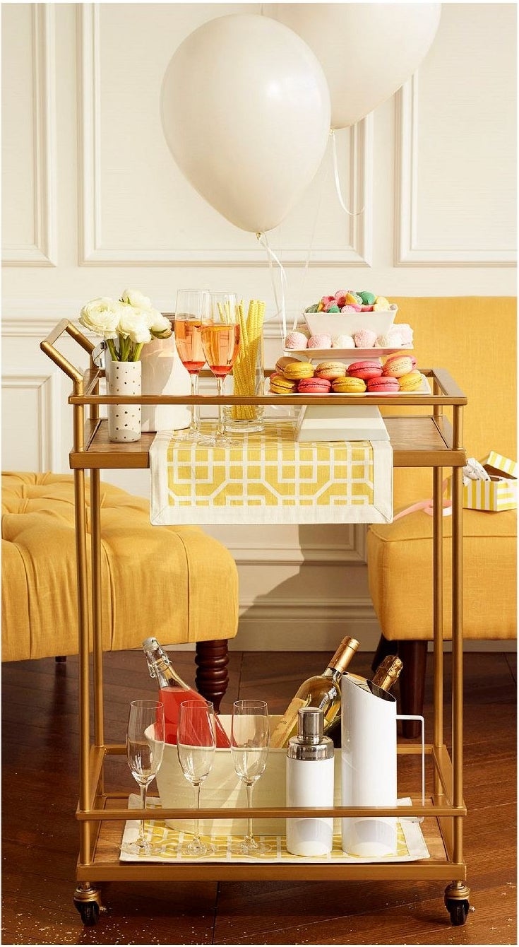a brass bar cart with a lower shelf and a top shelf in addition to wheels