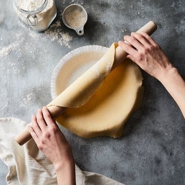 hands using the rolling pin to roll pie crust onto a pan