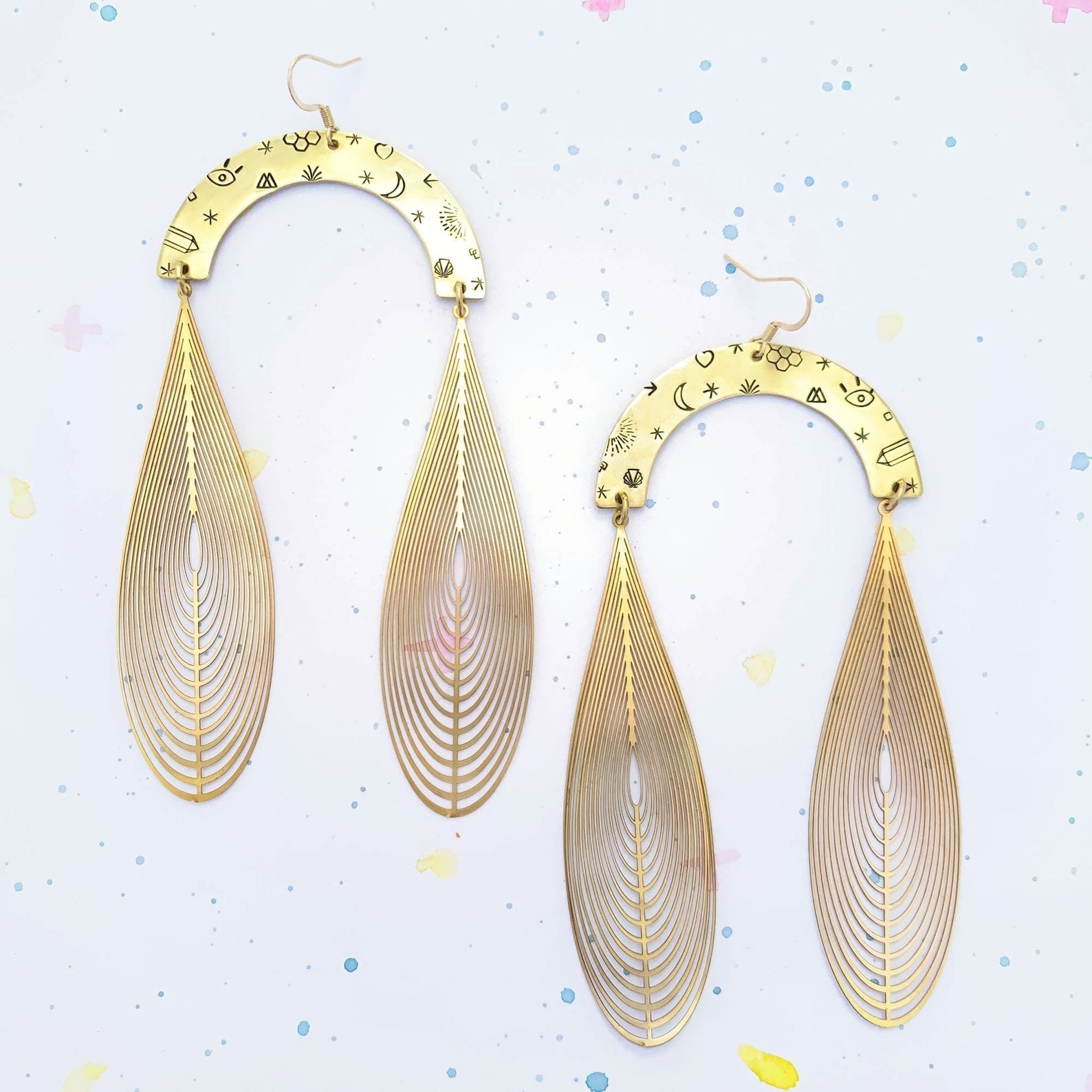 The earrings featuring an arch with a moon, eye, stars, and other symbols on it, with two gold  &quot;magic wings&quot; hanging from the arches 