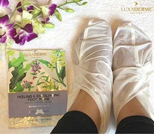 A pair of legs with the foot mask on them next to some flowers and a foot mask packet.