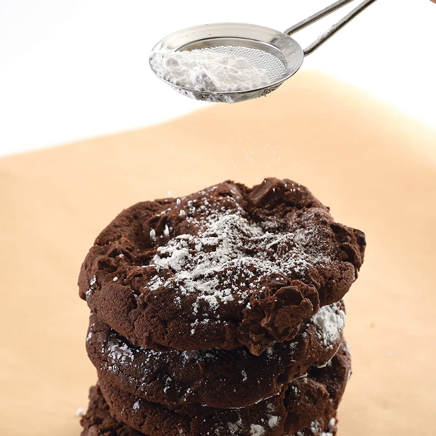 Powdered sugar is being sifted onto cookies from a sifter