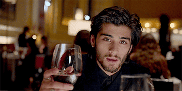 Zayn Malik clinking a glass of wine in One Direction&#x27;s music video &quot;Night Changes.&quot;