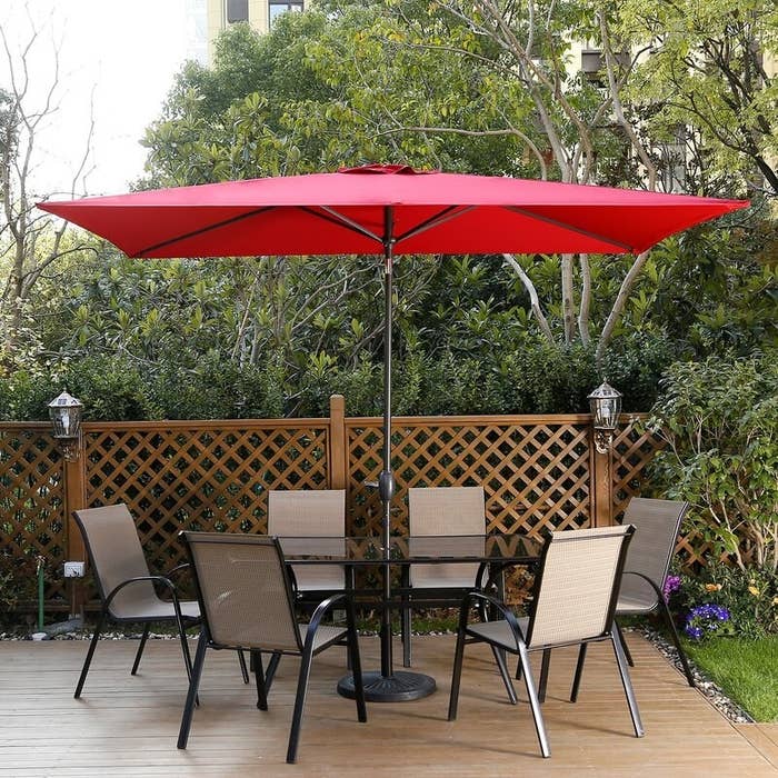 An umbrella sticking out of a table and providing shade for the table and six chairs