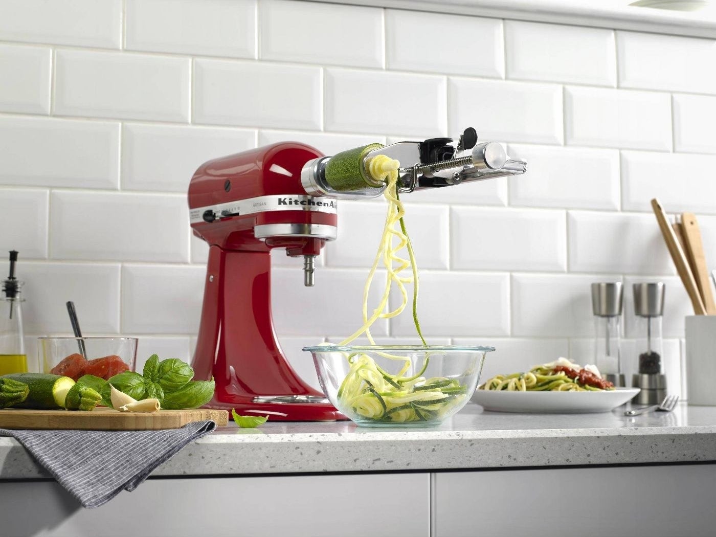 a red kitchen aid mixer with the stainless steel attachment making zucchini noodles