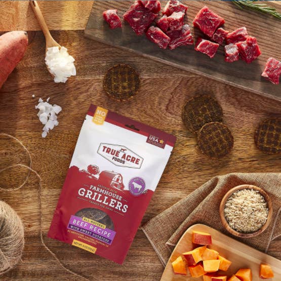 treat bag on a table with the round waffle texture looking treats around raw versions of the ingredients like beef and sweet potatoes