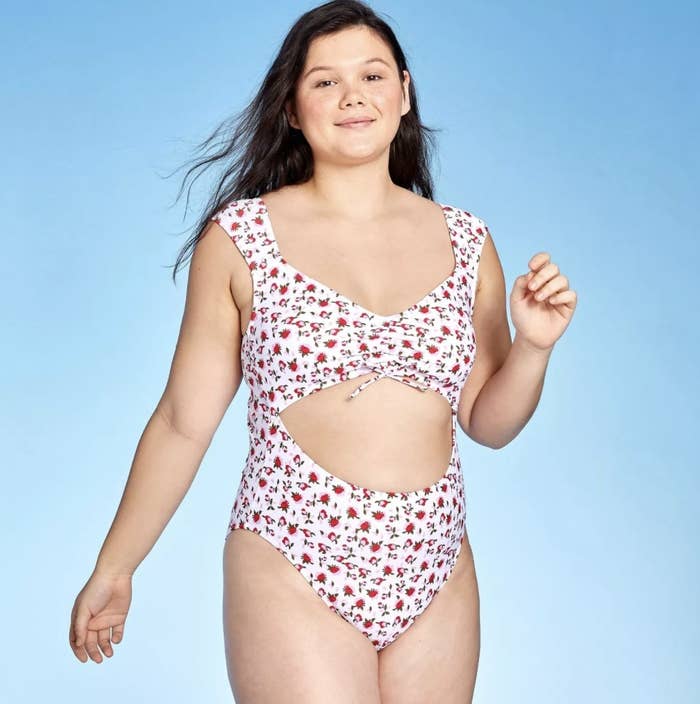A model in a white one piece with floral detailing and a cut out at the rib 