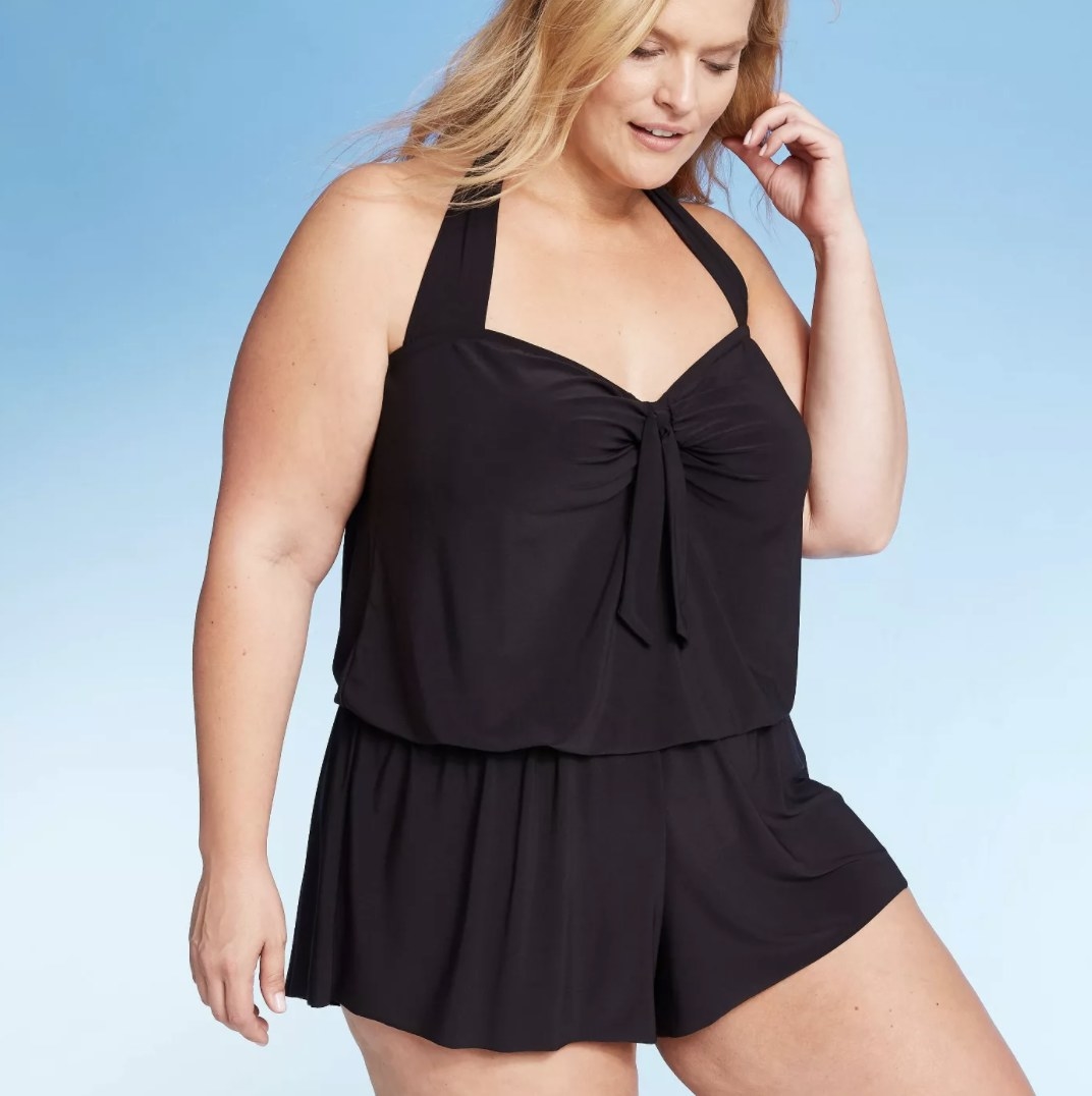 A model in back a swim romper that cinches at the lower waist and has a bow at the chest 
