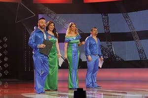 Four people standing on a Eurovision stage in plastic outfits