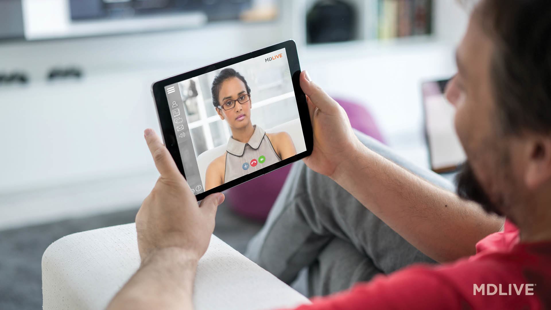 A person holds their tablet, video conferencing with their therapist from an arm chair