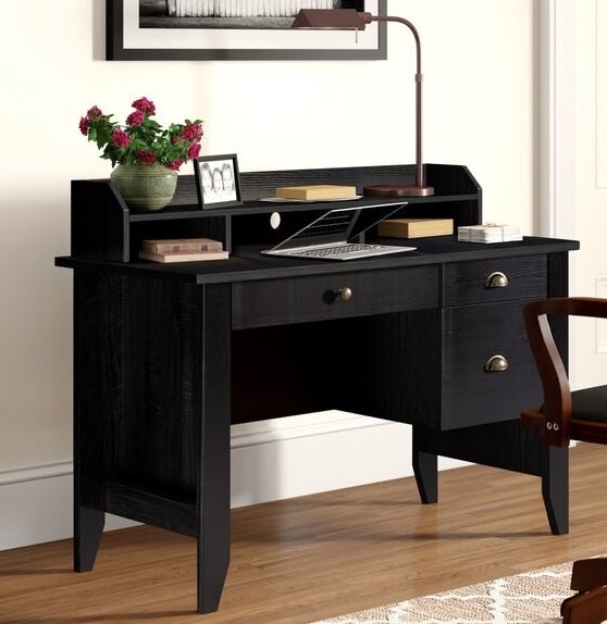 A black desk with three drawers, three cubbies, and one shelf